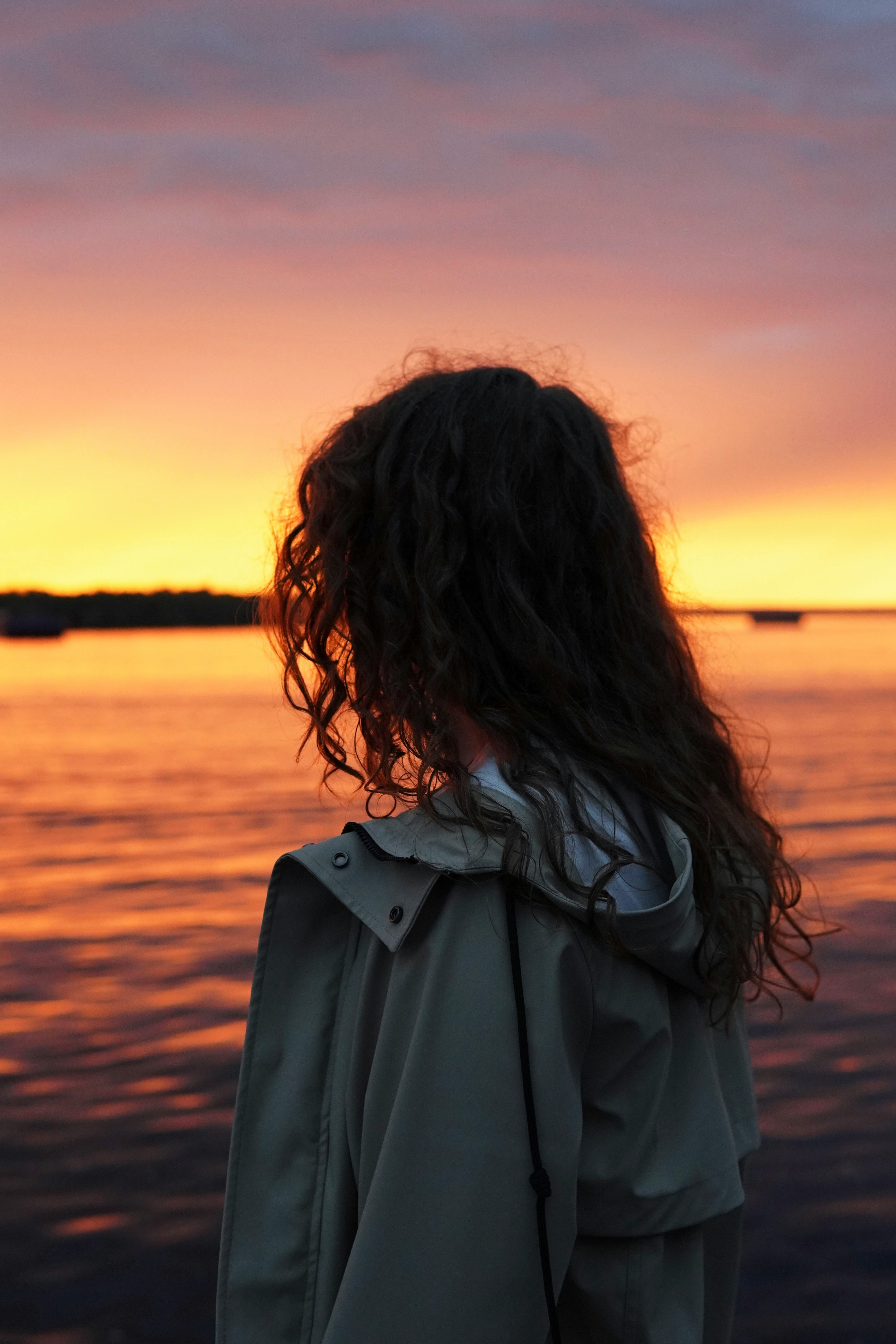 woman in gray coat standing on seashore during sunset